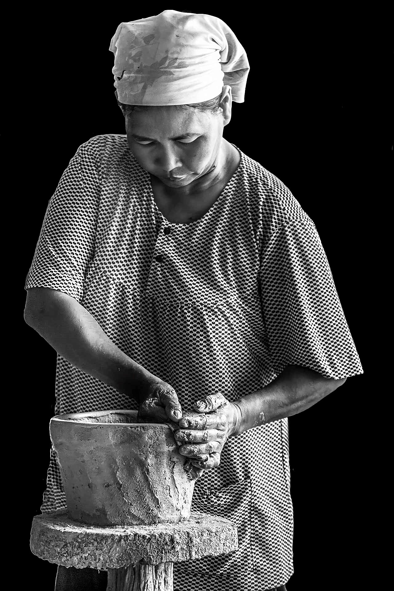 Ảnh đen trắng: người thợ nữ khăn trùm đầu, hai bàn tay lấm đất vuốt thân bình trên bệ